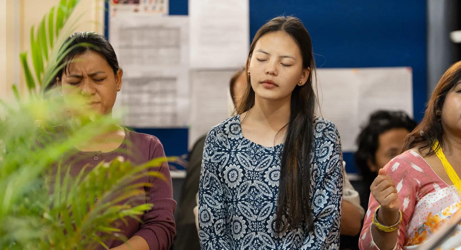 Young women and men standing with their eyes closed in quiet prayer during worship.